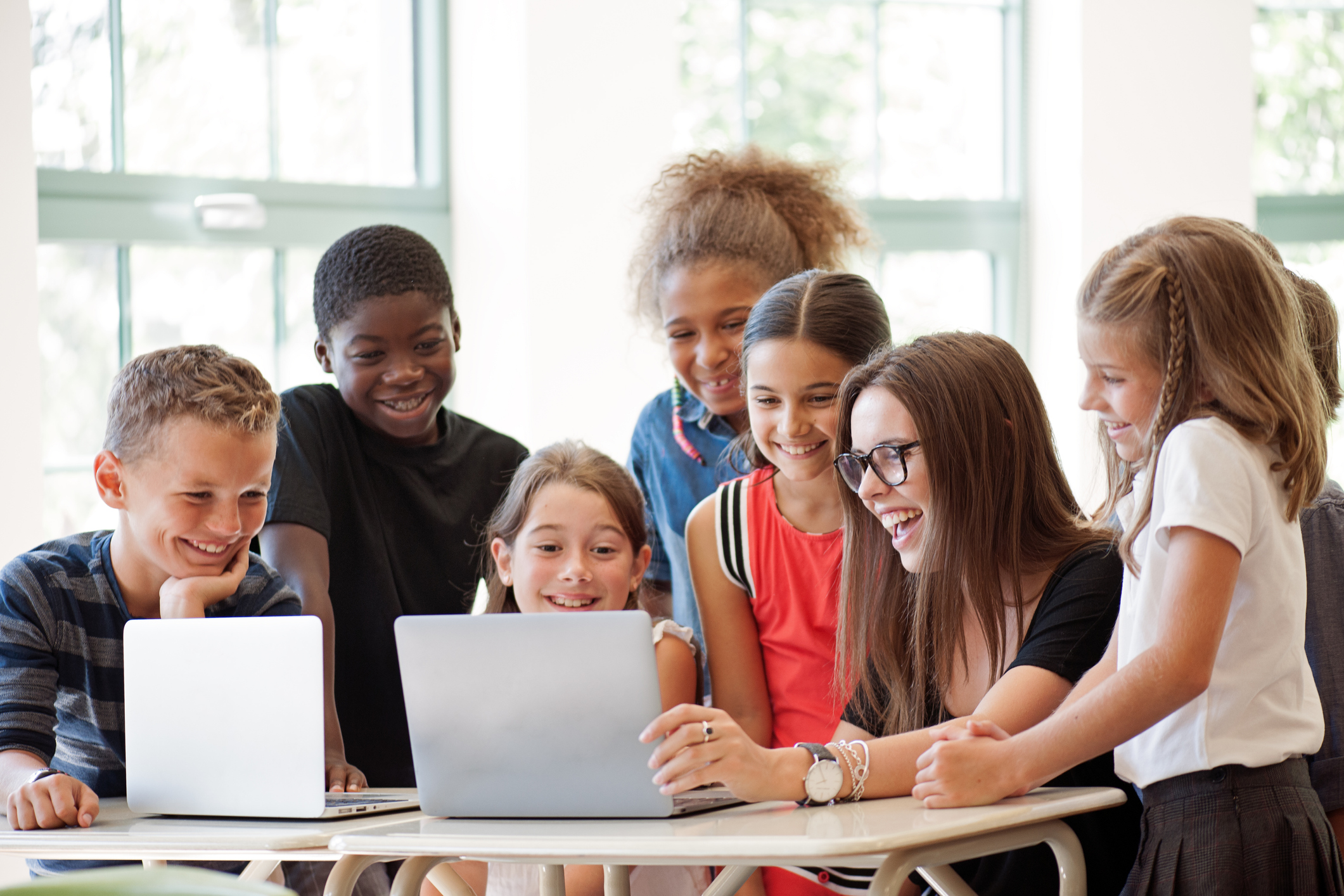 School children using laptop with teacher in the classroom.
