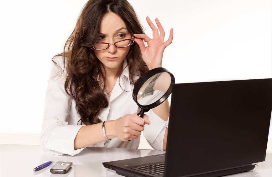 women using magnifying glass to view computer, as if she is suspicious